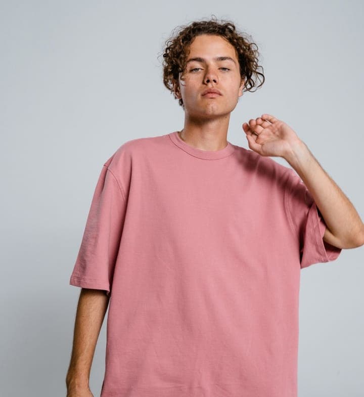 A curly-haired young man in a pink T-shirt