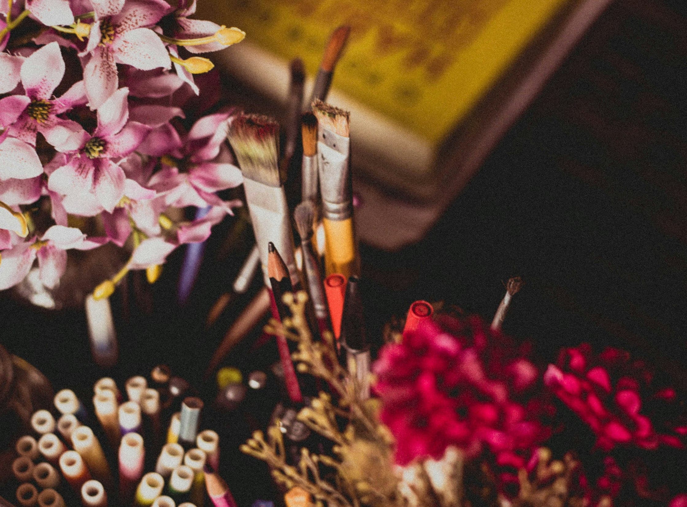 Paintbrushes and markers in a jar beside pink flowers