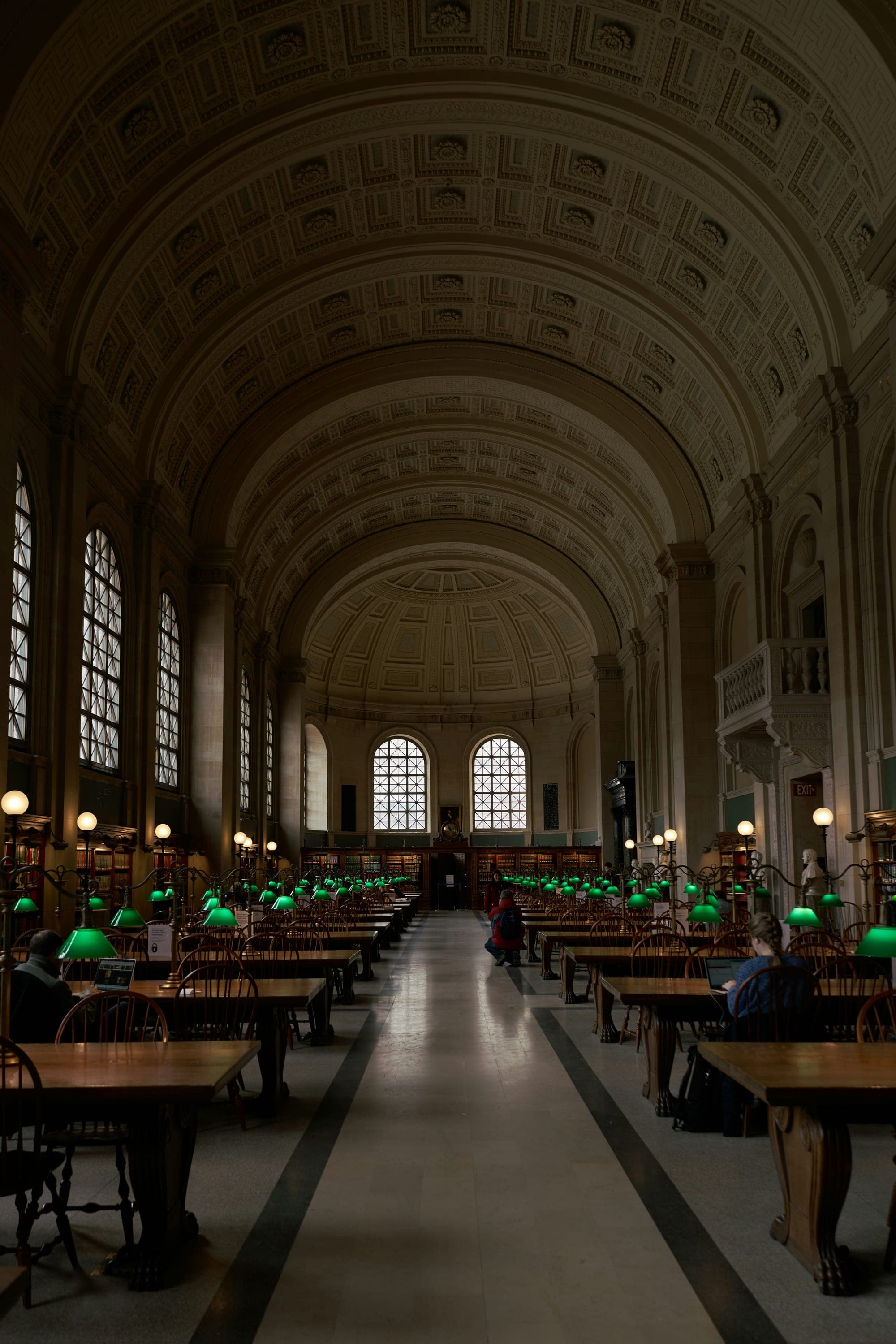 A long reading room with arched ceilings, tables and green lamps