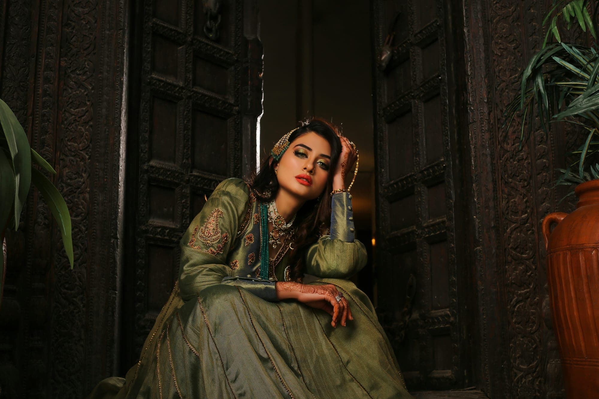 A woman in an embroidered green dress seated before a carved door