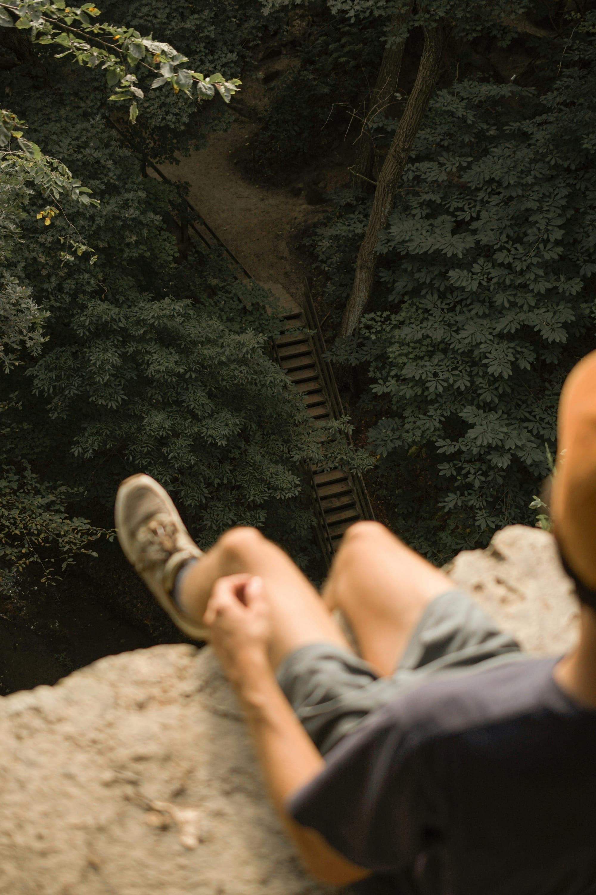 Legs of a person sitting on a rock above a forest trail