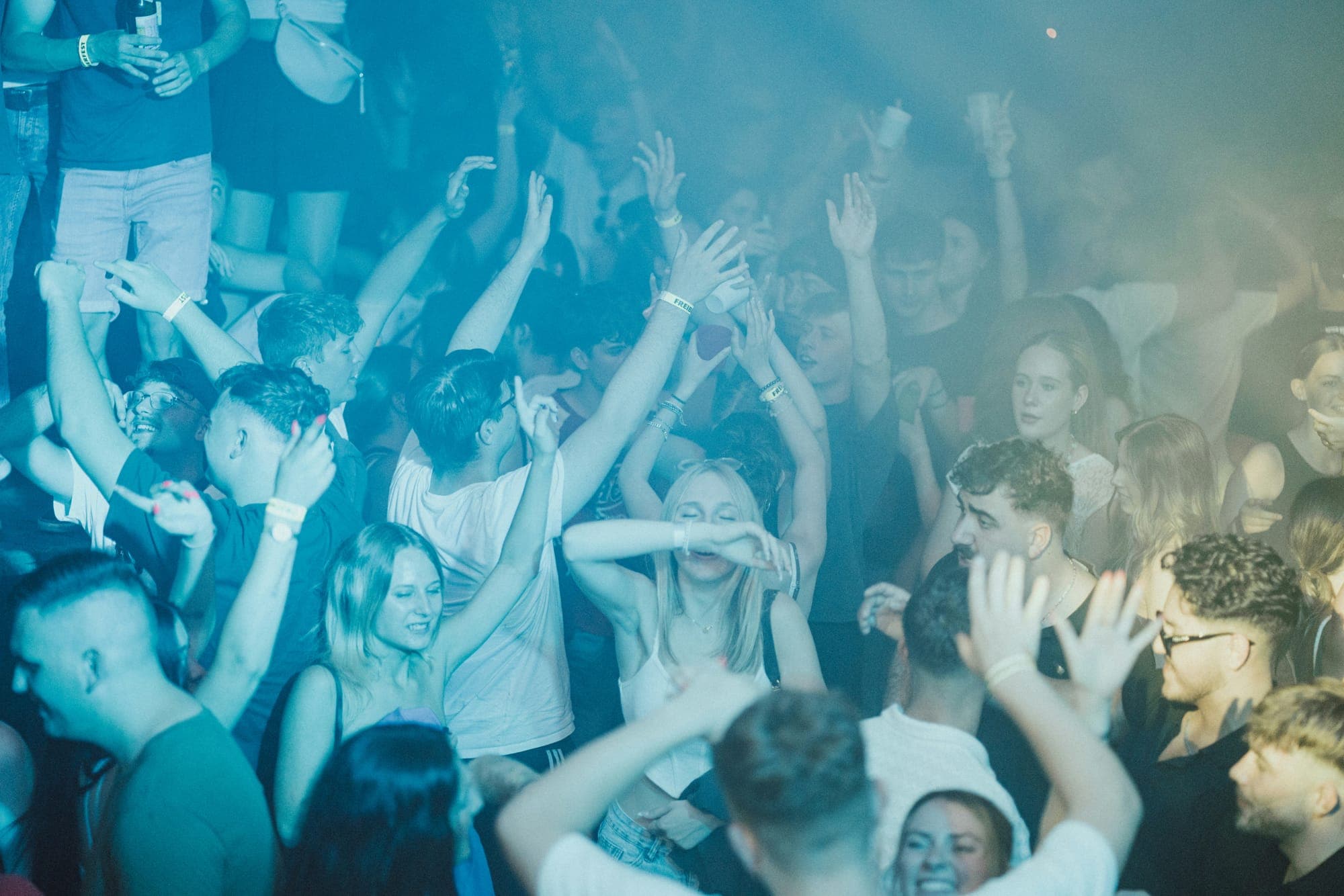 A crowd dancing with raised arms under blue concert lights