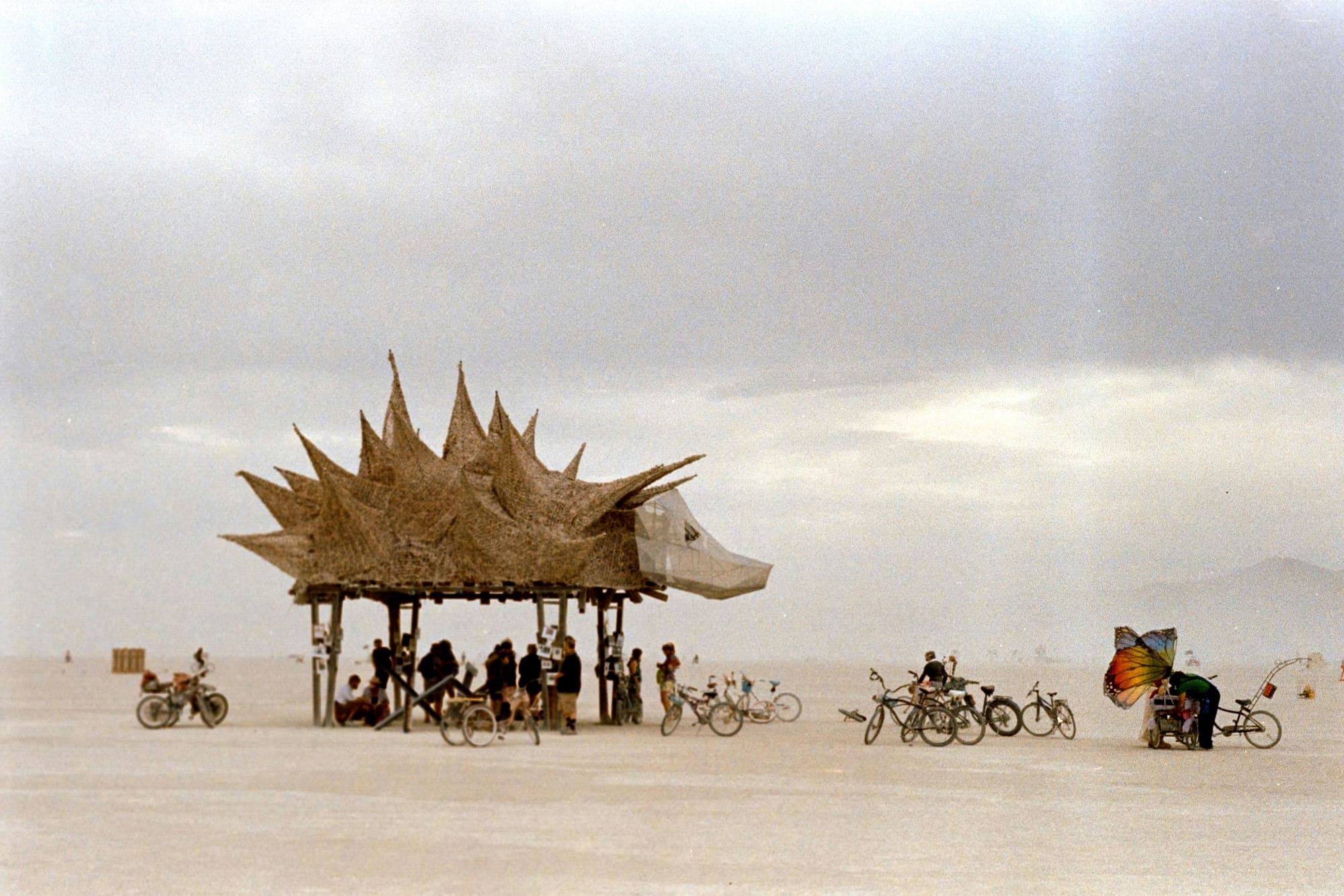 A spiky wooden art structure in a desert with bicycles around it