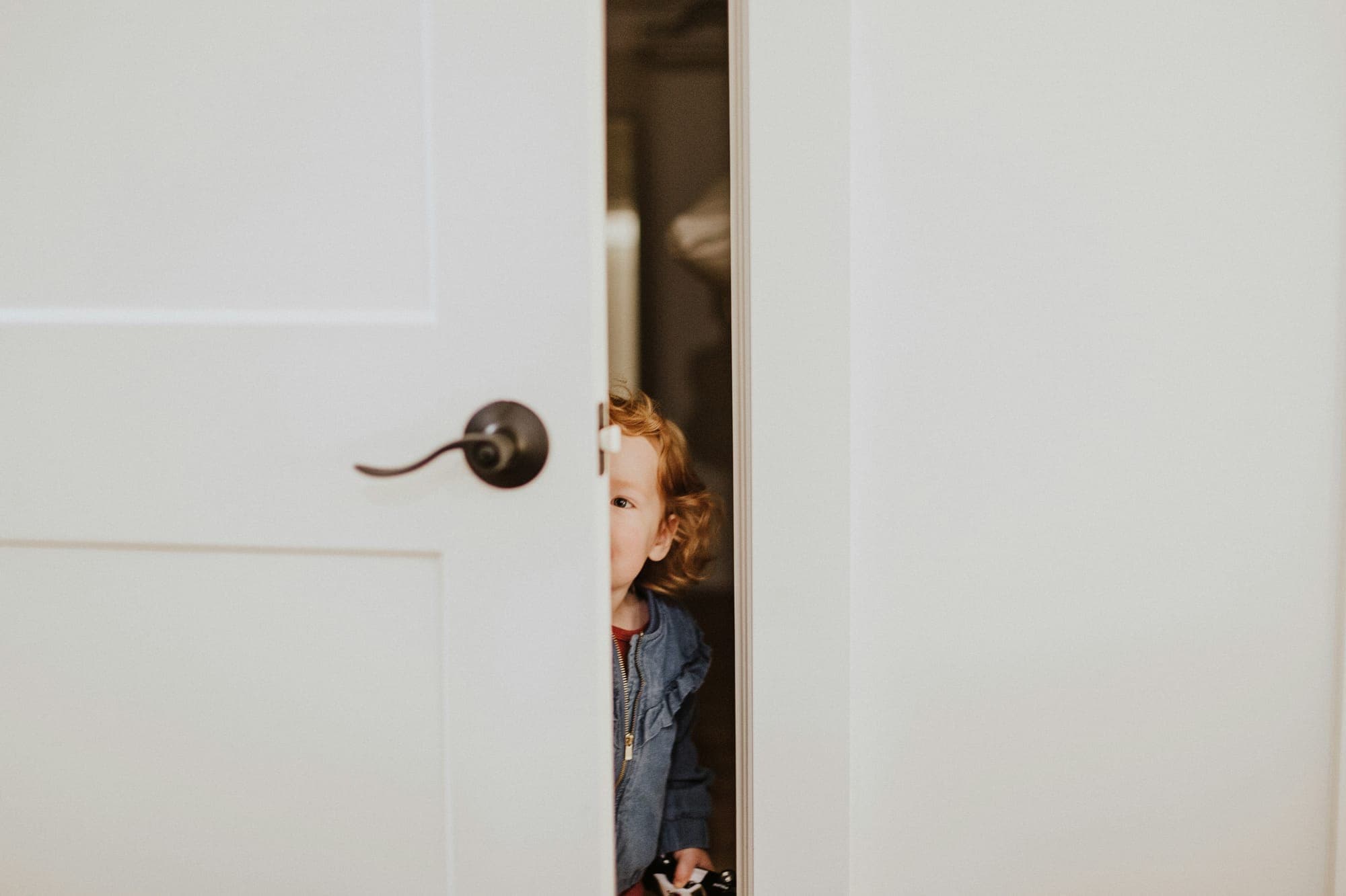 A small child peeking around a half-open white door