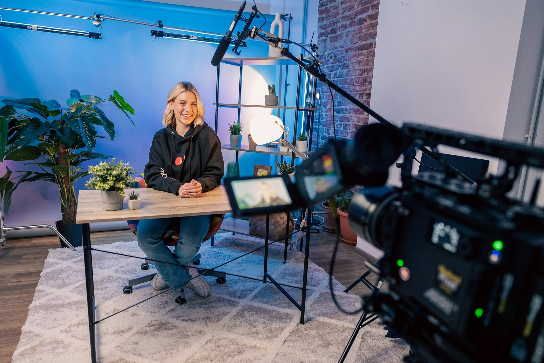 A woman at a desk in a studio facing a film camera